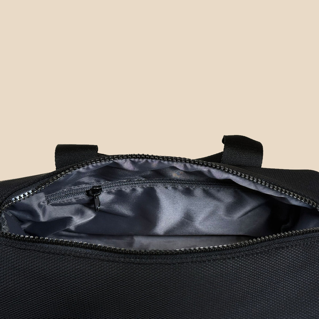 Close-up of an open black duffel bag showing a dark gray interior lining and a zippered pocket inside