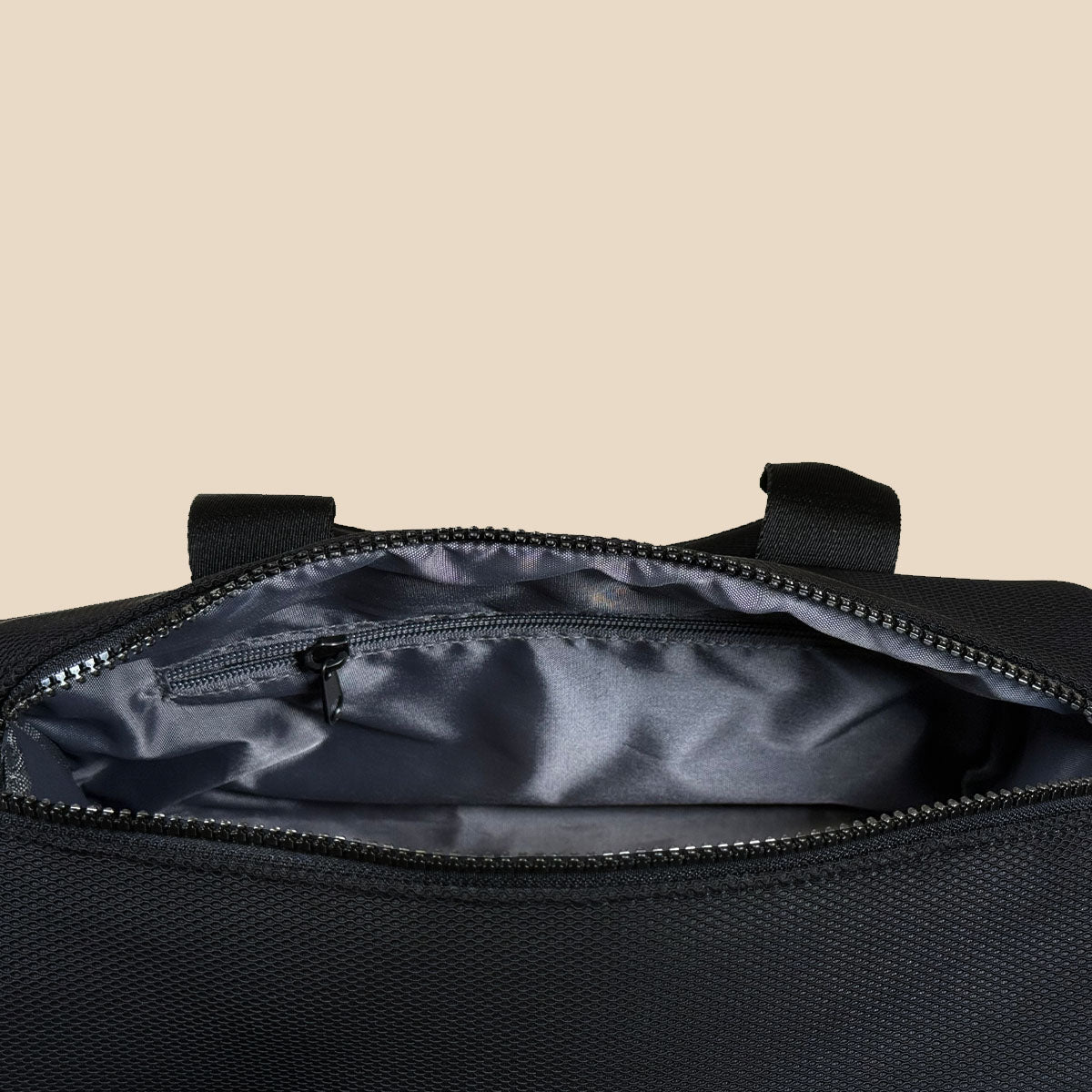 Close-up of an open black duffel bag showing a dark gray interior lining and a zippered pocket inside