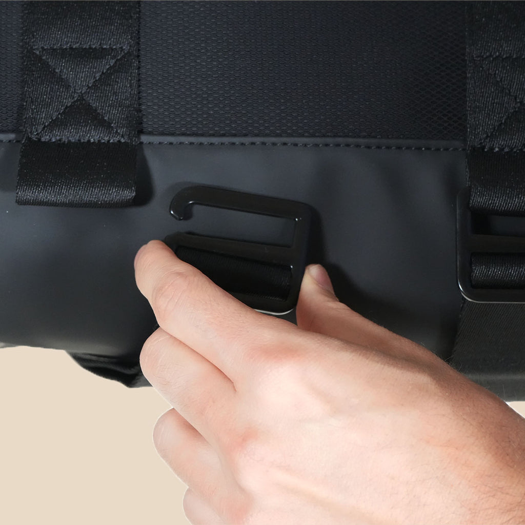 A close-up of a person's hand adjusting the bottom strap quick-release buckle on the black orion mini duffel bag