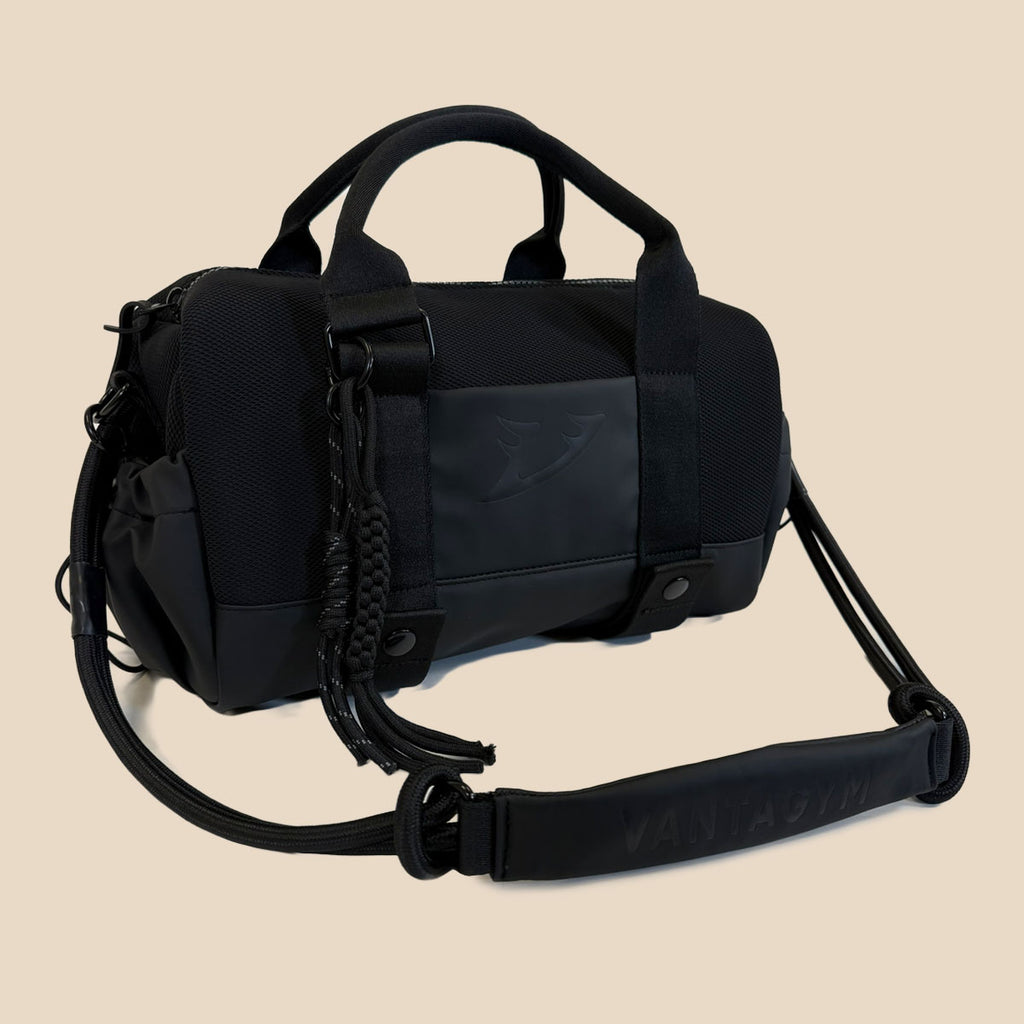 Vantagym Orion black mini duffel bag with dual top handles, a detachable shoulder strap, and a braided tassel detail