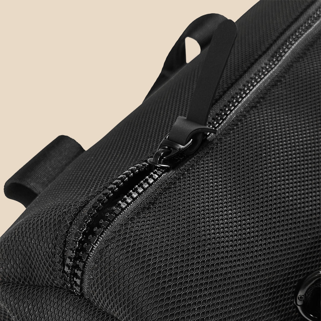 Close-up of a black textured mesh bag with a black zipper and pull tab, set against a solid beige background.